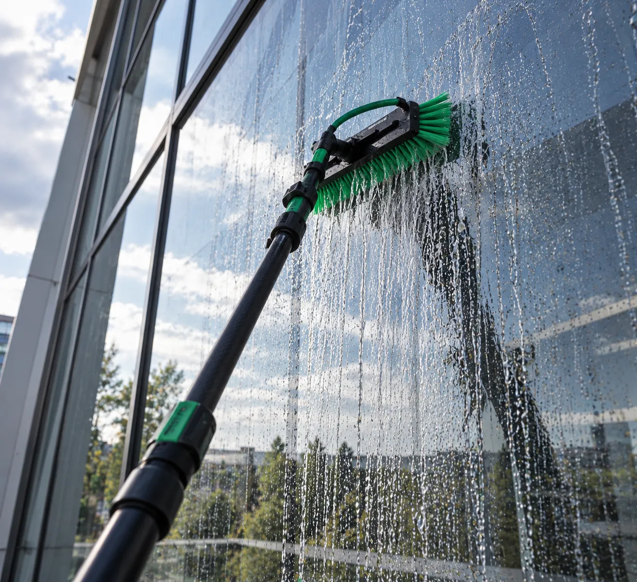 Wasserführende Teleskopstange mit Bürste reinigt eine Glasfassade mit Reinwasser